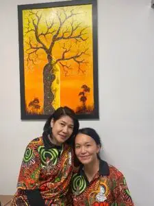 Imelda and Eileen facing the camera in front of a painting.