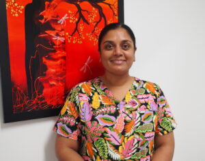 Sarah smiling at the camera in front of a colourful painting.